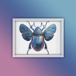 May include: A framed cross-stitch depicting a blue beetle with open wings. The beetle features intricate details in shades of blue, purple, and gold. The artwork is set against a white background and framed in a white border.