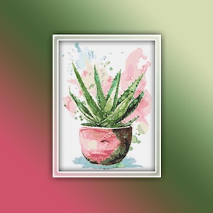 以下が含まれることがあります： 白い背景にピンクとブルーの水彩の飛沫が描かれた、ピンクの鉢に入った緑のアロエの植物の水彩画です。