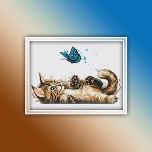 May include: A brown and white kitten lies on its back with its paws in the air, looking up at a blue butterfly flying above. The background is white with watercolour-like blue splatter.