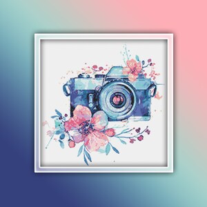 Könnte beinhalten: Eine Vintage-Kamera in Blau und Silber ist von rosa und blauen Aquarellblumen umgeben. Die Kamera hat ein großes Objektiv und einen schwarzen Riemen.