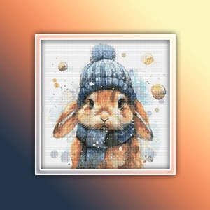 May include: A brown rabbit wearing a blue knit hat with a white pom pom and a blue scarf. The rabbit is surrounded by a watercolor background with white dots.