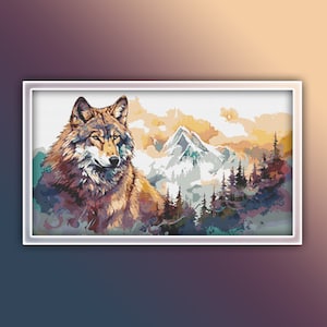 May include: A framed cross-stitch artwork shows a wolf with brown and grey fur, looking to the side. The background features a mountain range, pine trees, and a sunset with orange and yellow hues. The artwork is framed in a white border.