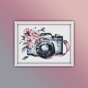 May include: A vintage camera with a pink floral design. The camera is gray with a black lens and a pink ribbon.