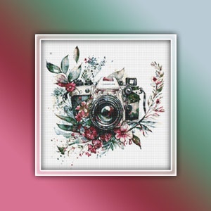 Könnte beinhalten: Eine Vintage-Kamera mit einem schwarzen Objektiv, umgeben von einem Aquarell-Blumenarrangement mit rosa, grünen und weißen Blüten.