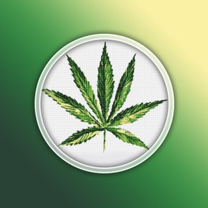May include: A green marijuana leaf embroidered on white fabric in a round embroidery hoop.