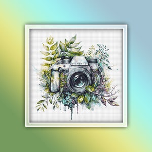 May include: A vintage camera surrounded by green and blue watercolor leaves and flowers. The camera is silver and black with a lens in the center.