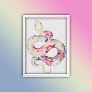 Puede incluir: Un punto de cruz enmarcado de una serpiente con un patrón floral en rosa, crema y azul. La serpiente está enrollada y centrada dentro de un marco blanco, sobre un fondo degradado de rosa, amarillo y azul.