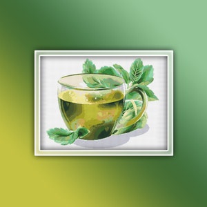 May include: A glass cup filled with green tea, surrounded by green leaves. The cup is sitting on a white background.