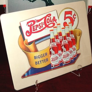 以下が含まれることがあります： 赤色のペプシコーラロゴ、5セントの価格タグ、ペプシのボトルが特徴のヴィンテージペプシコーラの看板。看板はクリーム色の背景に「BIGGER BETTER」と書かれた黄色のバナーが付いています。