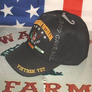 May include: Black baseball cap with embroidered text and a military emblem. The cap features the words "Vietnam Vet" and "Combat Veteran" in gold thread. The back of the cap has the text "38479 GAVE ALL".