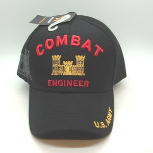 May include: Black baseball cap with embroidered text and graphics. The cap features the words "COMBAT ENGINEER" in red, along with a gold and black emblem. The text "U.S. ARMY" is embroidered in gold on the side. A tag is attached to the cap.