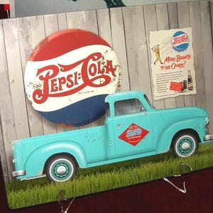 May include: A vintage-style metal sign featuring a light blue pickup truck with the Pepsi-Cola logo. The sign includes a large circular Pepsi-Cola emblem and a smaller advertisement with the text "More Bounce to the Ounce!"