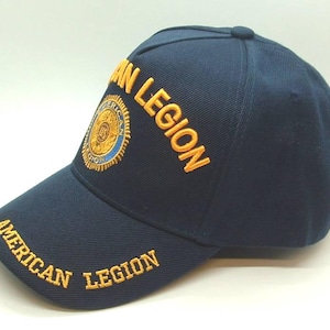 May include: Navy blue baseball cap with the words "AMERICAN LEGION" embroidered in gold on the front and bill. The cap features a circular patch with gold and blue detailing.