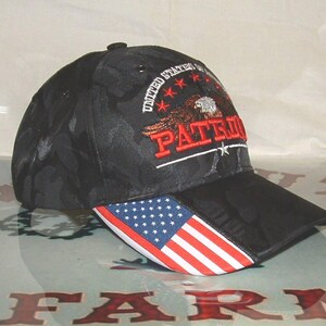 Pode incluir: Boné de beisebol preto com padrão de camuflagem. O boné apresenta um design bordado com uma águia, a palavra "PATRIOT" em vermelho e o texto "UNITED STATES OF AMERICA". A aba exibe a bandeira americana.