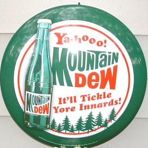 May include: A vintage Mountain Dew sign. The round sign features a green border with the Mountain Dew logo in the center, along with a bottle graphic. The text reads "Ya-hooo! Mountain Dew. It'll Tickle Yore Innards!"