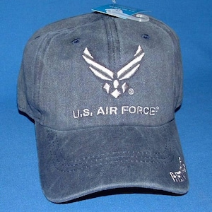 May include: Navy blue baseball cap with the U.S. Air Force logo embroidered in white. The text "U.S. AIR FORCE" is embroidered below the logo. The cap has a curved brim and a tag attached to the top.