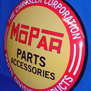 May include: A circular metal sign featuring a yellow center with the red MOPAR logo and black text reading PARTS ACCESSORIES. The red border displays white text reading THE CHRYSLER CORPORATION and PARTS DIVISION PRODUCTS in a bold font.