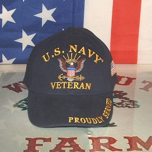Könnte beinhalten: Eine marineblaue Baseballkappe mit goldener Stickerei, die vorne U.S. NAVY VETERAN und auf dem Schirm PROUDLY SERVED zeigt. Ein Adleremblem mit Schild und Anker ist mittig platziert, und eine kleine amerikanische Flagge befindet sich an der Seite.