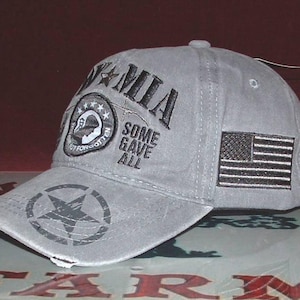 May include: Gray baseball cap with a distressed look, featuring the text "POW MIA" and an American flag patch. The cap also has a star graphic and the words "Some Gave All".