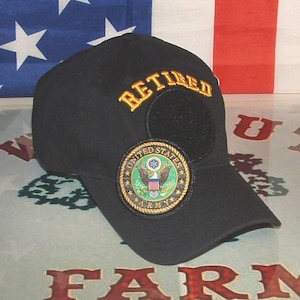 May include: Black baseball cap with gold embroidered "RETIRED" text above a circular patch. The patch displays the United States Army emblem in green, gold, and blue. The cap has a curved peak and a hook-and-loop fastener patch.