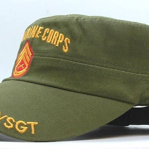 May include: Olive green military-style cap with a flat brim. The cap features embroidered text "MARINE CORPS" and "GYSGT" in gold, along with a red and gold emblem. A classic military-inspired accessory.