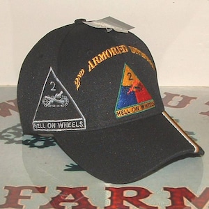 Peut inclure: Casquette de baseball noire avec des écussons brodés. Comprend le texte "2nd ARMORED DIVISION" et "HELL ON WHEELS". La casquette a une visière incurvée avec une rayure blanche et beige.