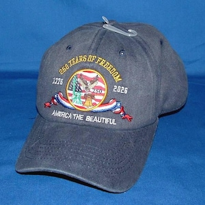 Könnte beinhalten: Marineblaue Baseballkappe mit gesticktem Design. Das Design enthält den Text "250 Years of Freedom" und "America the Beautiful" sowie ein Emblem mit einem Adler, einer Glocke und den Jahren 1776 und 2026.