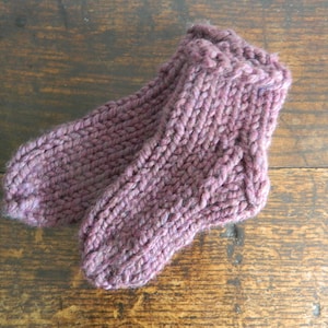 May include: A pair of hand-knitted socks in a deep purple color. The socks are made with a simple knit stitch and have a ribbed cuff.