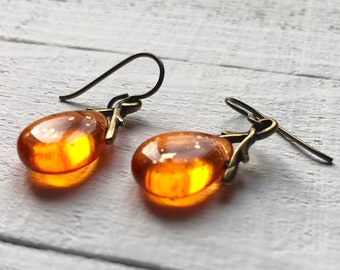 May include: A pair of amber glass earrings with a gold-toned twig design. The earrings are teardrop shaped and have a shiny finish.