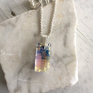 May include: A silver chain necklace with a rectangular iridescent crystal pendant.