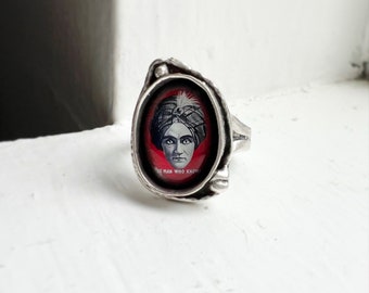 Op de afbeelding: Een zilveren ring met een ovale bezel met een vintage illustratie van een man met een tulband met de tekst "The Man Who Knows".