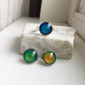 May include: A set of three mood rings, one ring and two earrings. The ring is silver with a blue mood stone. The earrings are silver with green and orange mood stones.