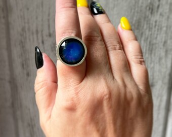 Puede incluir: Un anillo de plata con una piedra redonda azul iridiscente engastada en un engaste de plata.