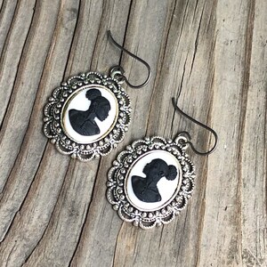 May include: A pair of silver earrings with a black silhouette cameo of a woman in a white oval frame.