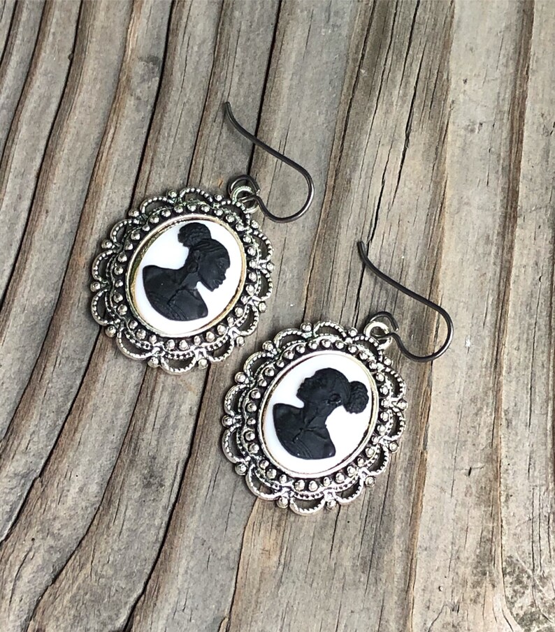 May include: A pair of silver earrings with a black silhouette cameo of a woman in a white oval frame.