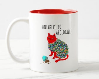 Peut inclure: Une tasse en céramique blanche avec un bord rouge. La tasse représente un chat de dessin animé portant une guirlande colorée et le texte "UNLIKELY TO APOLOGIZE".