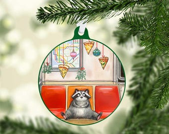 Peut inclure: Une décoration de Noël ronde avec une bordure verte et un ruban blanc. À l'intérieur, un raton laveur est assis sur un siège de métro, avec des tranches de pizza et du gui suspendus. Une carte du métro est visible en arrière-plan.