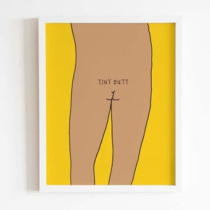 May include: A framed wall art print featuring a minimalist line drawing of a tan-colored lower torso against a solid yellow background. The illustration includes the hand-lettered black text "TINY BUTT" positioned directly above the line art detail.