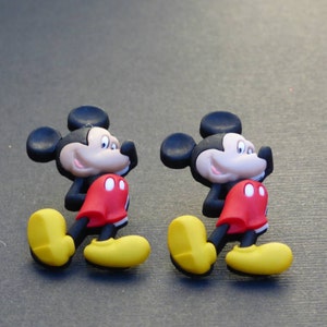 Może przedstawiać: Dwie plastikowe figurki Myszki Miki w kolorze czarnym, czerwonym i ż&oacute;łtym. Figurki są zwr&oacute;cone w prawą stronę obrazu i stoją na szarym tle.