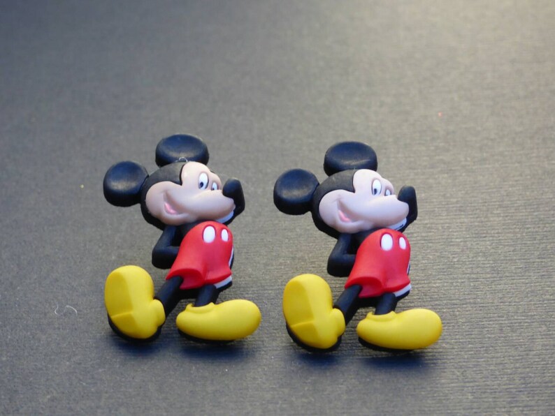 Może przedstawiać: Dwie plastikowe figurki Myszki Miki w kolorze czarnym, czerwonym i ż&oacute;łtym. Figurki są zwr&oacute;cone w prawą stronę obrazu i stoją na szarym tle.