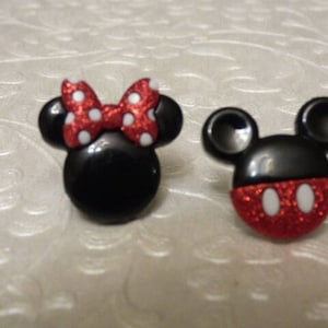 May include: A pair of black and red glitter Mickey Mouse and Minnie Mouse character buttons. Minnie Mouse has a red bow with white polka dots.