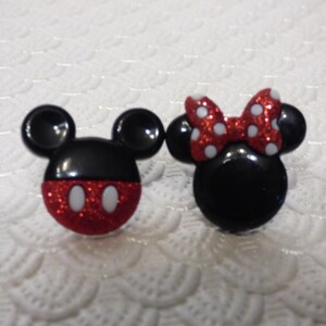 May include: A pair of red and black glitter Mickey Mouse and Minnie Mouse character earrings. The earrings are shaped like the characters' heads and have white polka dots.
