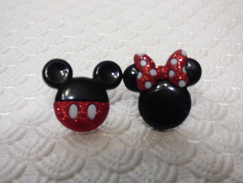 May include: A pair of red and black glitter Mickey Mouse and Minnie Mouse character earrings. The earrings are shaped like the characters' heads and have white polka dots.