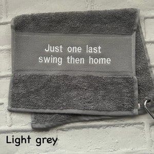 May include: Light grey towel with the text "Just one last swing then home" embroidered in white.