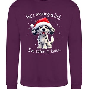 Puede incluir: Sudadera morada oscura con un dálmata de dibujos animados con un gorro de Papá Noel. El perro tiene manchas negras y está sonriendo. El texto de la camisa dice: "Está haciendo una lista, me lo he comido dos veces."