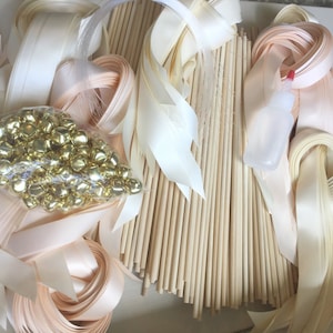 May include: A set of craft supplies for making ribbon wands, including wooden dowels, ivory and peach satin ribbon, and gold jingle bells.