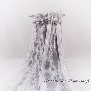 May include: Silver wedding ribbon wands with white feather trim and silver bells. The Brides Made Shop is printed on the bottom of the image.