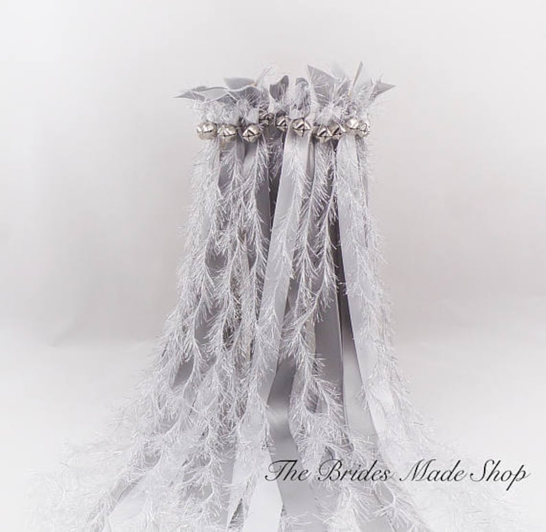May include: Silver wedding ribbon wands with white feather trim and silver bells. The Brides Made Shop is printed on the bottom of the image.