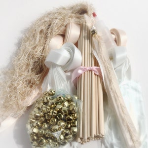May include: An assortment of craft supplies, including gold jingle bells in a clear bag, wooden dowels tied with pink ribbon, and various ribbons in white and cream colors. Also included are decorative feather plumes and a bundle of fluffy, light brown material.