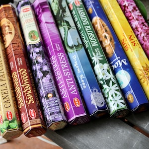 May include: A variety pack of incense sticks with different scents and colors. The scents include Cinnamon Patchouli, Sandalwood, Anti-Stress, Dragons Blood, Jasmine Blossom, Moon, Sun, and Lilac. The sticks are packaged in colorful boxes with images and text.